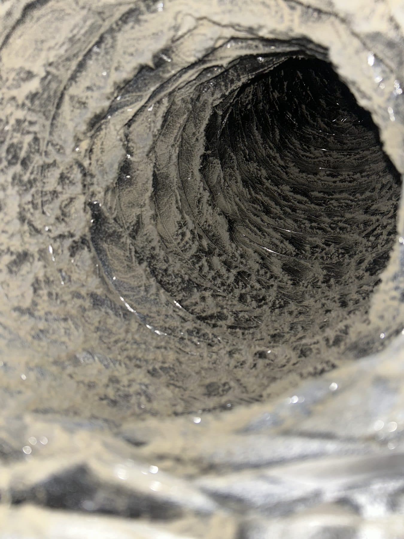 Heavy dust and debris built up along the ribs of a flexible duct interior