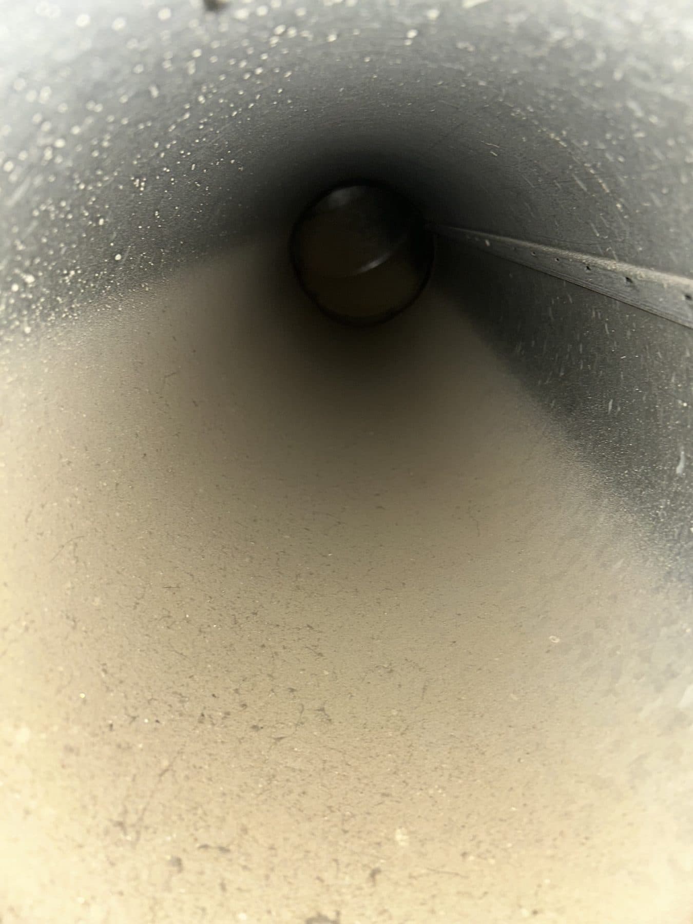 Interior of a rigid round duct trunk line with a film of dust across the metal